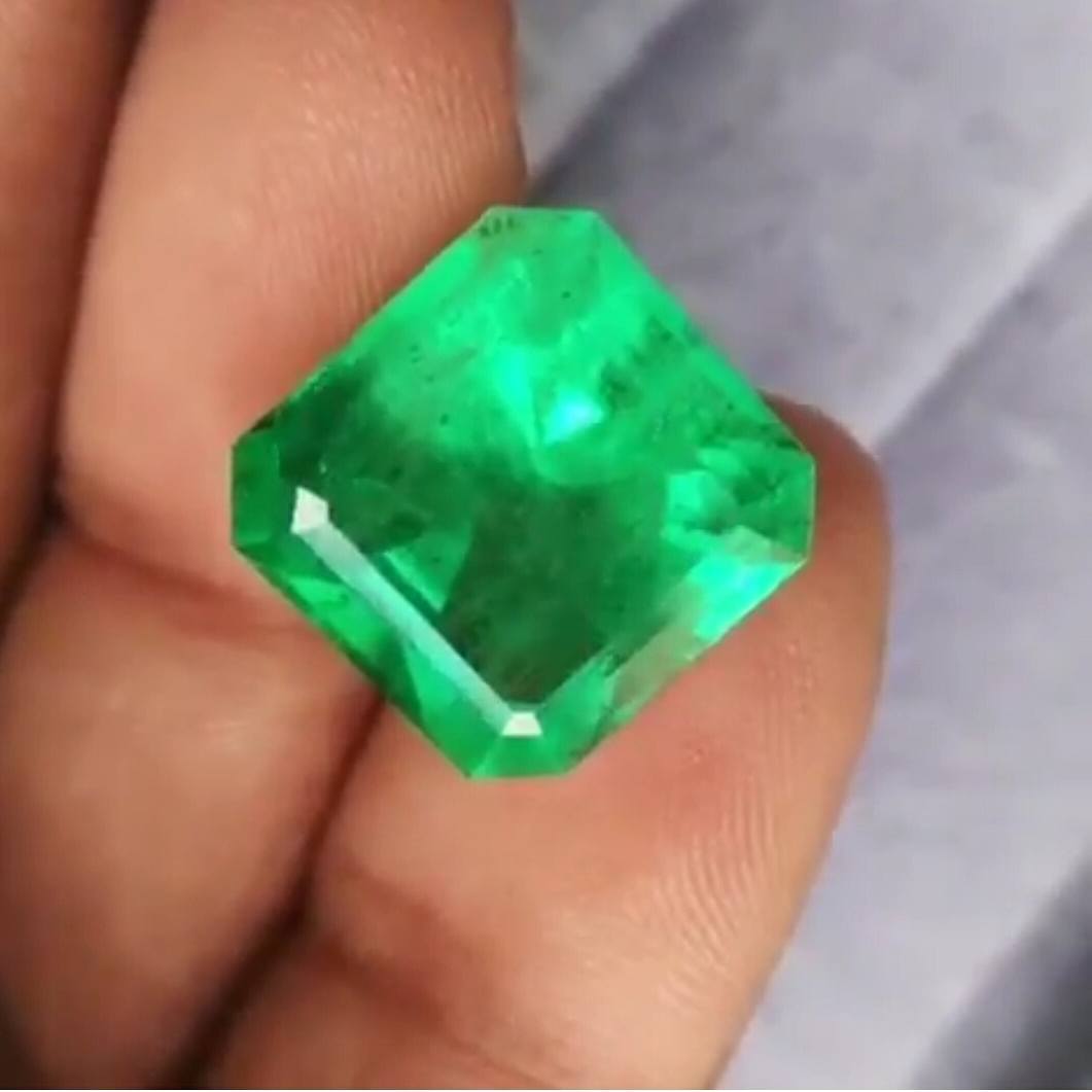 Square cut green emerald held by fingers